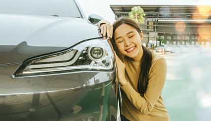 Beautiful Asian woman sitting on the side of the car in love and fascinated by EV electric car...