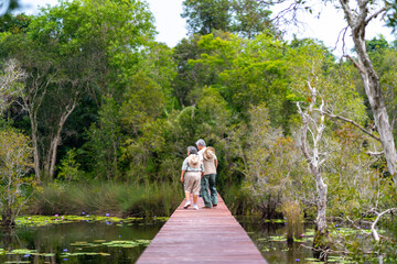Happy Asian senior couple walking on wooden bridge during hiking together at tropical forest. Retired elderly people man and woman enjoy outdoor lifestyle travel nature on summer holiday vacation.