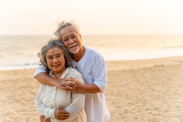 Portrait of Happy Asian family senior couple with gray hair walking together at tropical beach at summer sunset. Retired elderly people enjoy outdoor lifestyle travel nature ocean on holiday vacation.