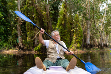Portrait of Happy Asian elderly man enjoy outdoor lifestyle kayaking at mangrove forest on summer vacation. Retired senior older people fun outdoor lifestyle travel nature rowing a boat in the river.