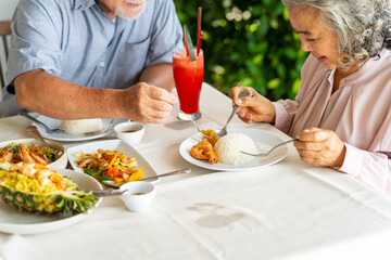 Happy Asian family senior couple having lunch and sharing meal together at restaurant. Elderly people man and woman enjoy retirement with outdoor activity lifestyle on summer holiday travel vacation.