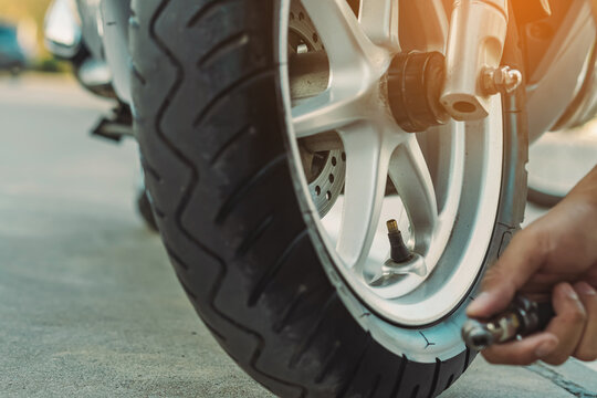 Hands Of Man Check Inflator Pressure And Inflates A Tire On Motorcycle With An Air Compressor. Man Checking Air Pressure And Filling The Tire Pressure On The Motorbike Wheel From Automatic Air Filler.