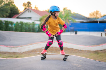Child or kid girl playing surfskate or skateboard in skating rink or sports park at parking to...