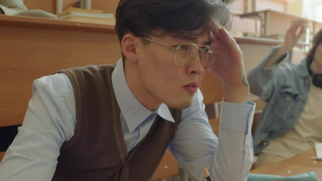 Selective focus tilt up shot of serious Asian college student ignoring annoying classmates trying to bully him
