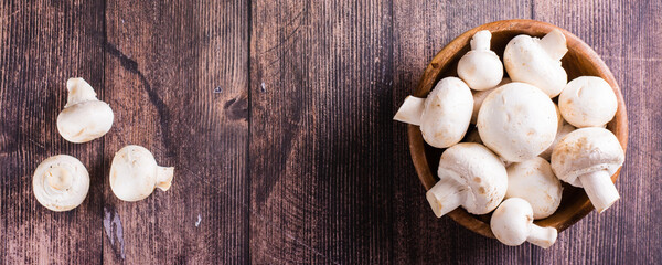 Fototapeta na wymiar Whole fresh champignons in a plate and on a wooden table top view web banner