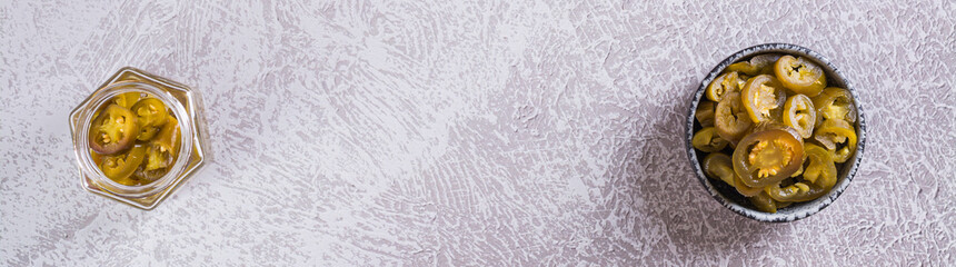 Spicy mexican pickled jalapeno peppers in bowl and glass jar top view web banner