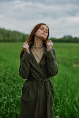 a beautiful woman stands in a green field and adjusts her coat