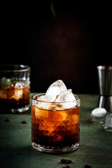 Black russian cocktail, alcoholic drink with vodka, coffee liqueur and ice, dark green background, bar tools