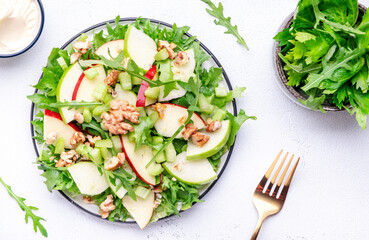 Waldorf salad with red and green apple, green celery, lettuce, arugula and walnuts on plate, white table background, top view