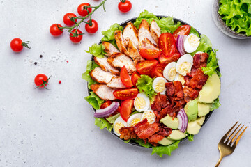 Cobb salad with chicken fillet, tomatoes, eggs, bacon, avocado and lettuce, gray table background, top view. American cuisine dish