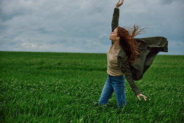 a woman in a coat stands in a field in cloudy weather resisting a strong wind