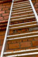 Aluminum ladder at the construction site against the background of a red brick wall. Work at height. Safety engineering.