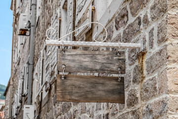 Two empty wooden old signs hang on chains against the background of a blurred stone wall of a building in the street, outdoors. Real vintage frame with copy space
