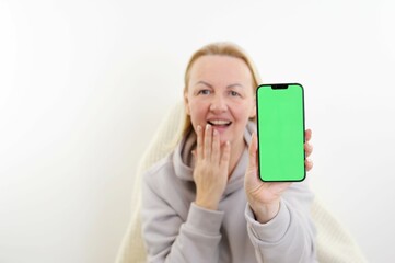 Young woman with surprise face points a finger to a smartphone with green screen in her hand. High...