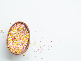 Sweet Easter concept. Chocolate easter egg with sweet sprinkles on white background with copy space. Design for a greeting card for the Easter holiday. Flat lay. Preparation for holiday.