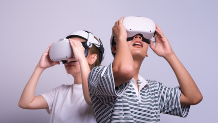 Surprised man and woman use vr glasses and looks at empty space with gray background. Virtual gadgets for entertainment, work, free time and study. Virtual reality metaverse technology concept.