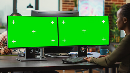 Young digital creator looking at computers with greenscreen, working on professional monitor with isolated display. Woman 3d editor analyzing blank chroma key mockup copyspace.