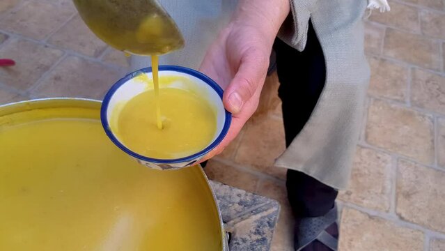 Close up shot of serving a golden sweet juicy drinking dessert halwa or halva Kaachi in a Persian enamel porcelain clay bowl by a Muslim woman hand in traditional house in Ardakan Yazd in Iran desert
