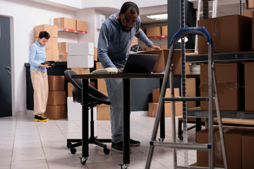 Warehouse employee analyzing transportation logistics on laptop computer before preparing customer packages, putting order in carton box. Supervisor working in storehouse delivery department