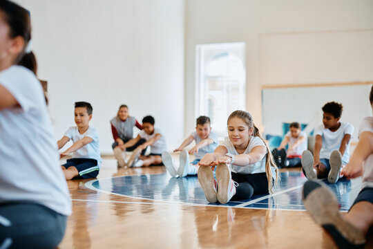 Schoolgirl and her classmates warming up during physical education class at school gymnasium.