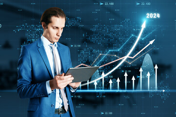 Attractive young businessman using tablet with growing business chart with arrow hologram on blurry...