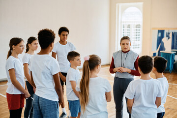 Young sports teacher talks to group of school kids during PE class.