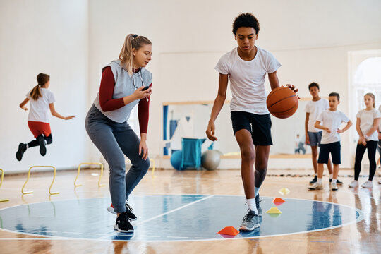 Black boy leading basketball during physical activity class at school gym.