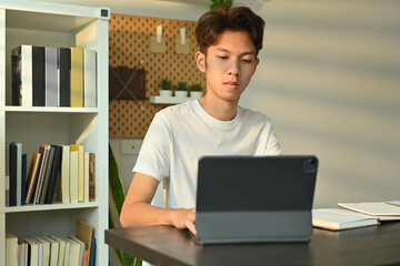 Young asian male looking at digital tablet, working or doing research or preparing for exam online. Education and technology