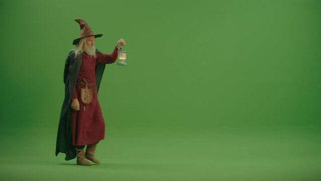 Green Screen. An Angry Old Wizard in a Magic Hat and in Medieval Clothing With a Lamp Walks and Looks Into the Distance. Magic Forest: a Mysterious and Mysterious World.