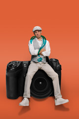 Depressed sad young photographer with lack of ideas and imagination sitting on camera, on an orange background