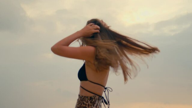 Beautiful long-haired girl twirling on the beach at sunset. Anamorphic shot