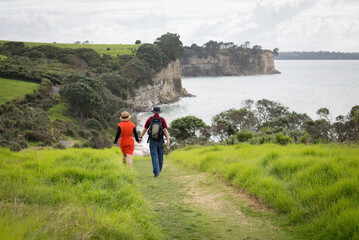 Obraz premium Couple holding hands, walking the Long Bay coastal walk. Auckland.