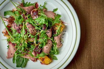 Salad with roast beef, arugula, caramelized onions in a plate on a wooden background