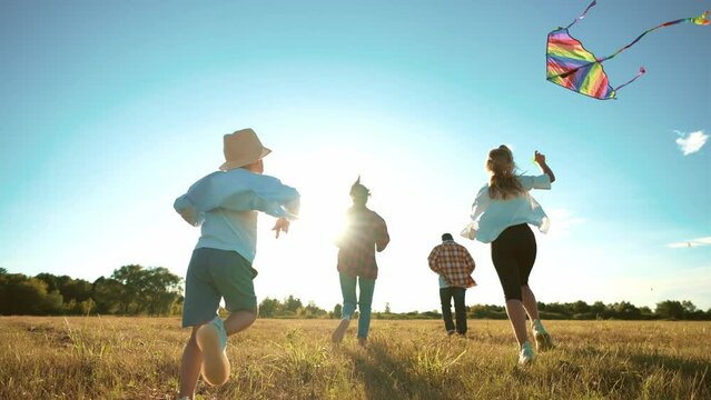 happy family running with kite flying in wind. Sports outdoors recreation in motion. Summer landscape. Parents play catch-up with children. Enjoy rest together. Leisure activity.