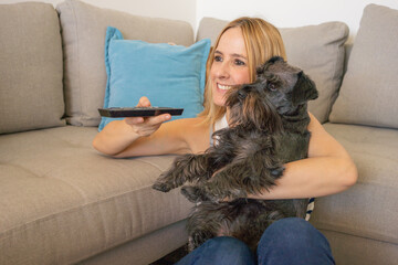 Young smiling woman with cute schnauzer dog watching TV at home