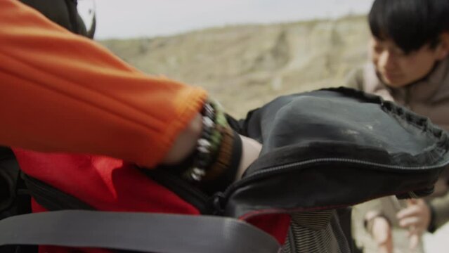 Close up of female hand oulling out package and book from rucksack in foreground. Blurred Asian woman and rocks un background