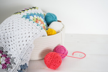 Fototapeta na wymiar granny sqaure blanket in white basket with woolen balls on white wooden ground handmade