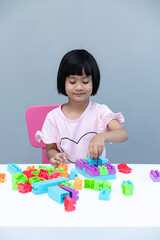 Happy asian little child girl playing a colorful block toy on table over white background. 
