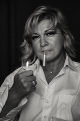Black white portrait of middle aged 45 years old woman lighting cigarette at black background. Thoughtful sad alone mature lady in white, aging image. Loneliness emotion concept. Copy ad text space