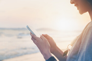 Woman traveling standing on the beach with hand holding smartphone with using social media on internet. Summer lifestyle.
