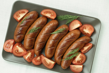 Grilled sausage with the addition of herbs and vegetables on the grill plate, outdoors. Grilling food, bbq, barbecue