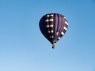 Naklejka premium Dark blue hot air balloon with people in basket flying in air and cloudless blue sky