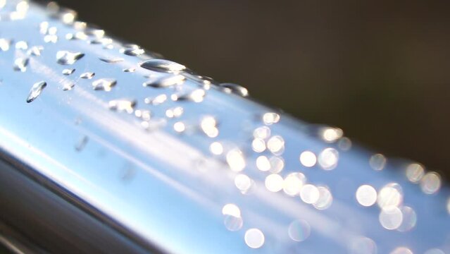 Raindrops on a stainless steel handrail in the park against a blurred bokeh light. Close-up shot. Water droplets from rain dew collecting on a shiny steel chrome pole hand rail railing.