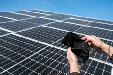 Hands holding black wallet empty without dollars over solar panels.