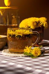 Dandelion flower healthy tea in glass teapot and glass cup on table. Delicious herbal tea from fresh dandelion flowers at home at summer day. Green clearing Hot dandelion tea in a glass teapot
