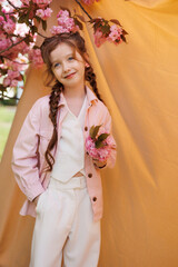 Playful girl in a good mood on a beige background and a branch of blooming sakura.