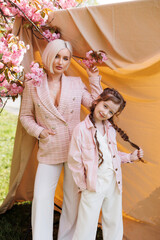 Beautiful mom with cute daughter in pink clothes standing in the park near the sakura, which bloomed with pink flowers in spring. Sakura blossomed.