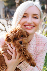 Pretty woman with a MALTIPOO dog. Adorable toy MALTIPOO puppy in arms of its loving owner. Small adorable doggy with funny curly fur with adult woman.