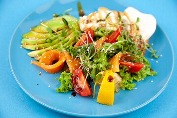 Healthy breakfast. Avocado and salmon, poached egg and toast, salad and vegetables. Microgreens on a plate. Food bowl. Lunch on a blue plate. Sauce and sesame seeds, lemon tomatoes. Top view.