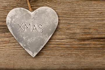 grey metal heart on rustic brown wooden background with free space for text and the letters XMAS